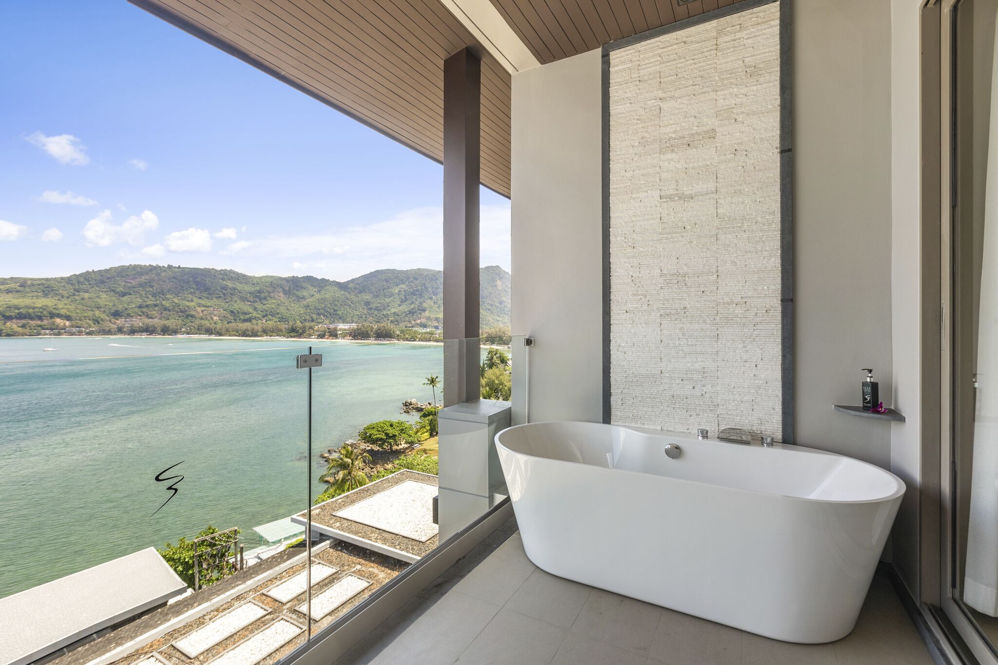 A modern bathroom with a freestanding bathtub, a large window, and a view of a body of water and hills.