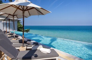 Zona de piscina con sillones y sombrillas, con vista a un océano azul y despejado.