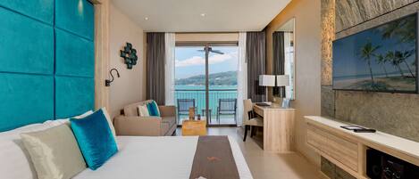 A hotel room with a bed, a desk, a TV, and a balcony with a view of the sea.