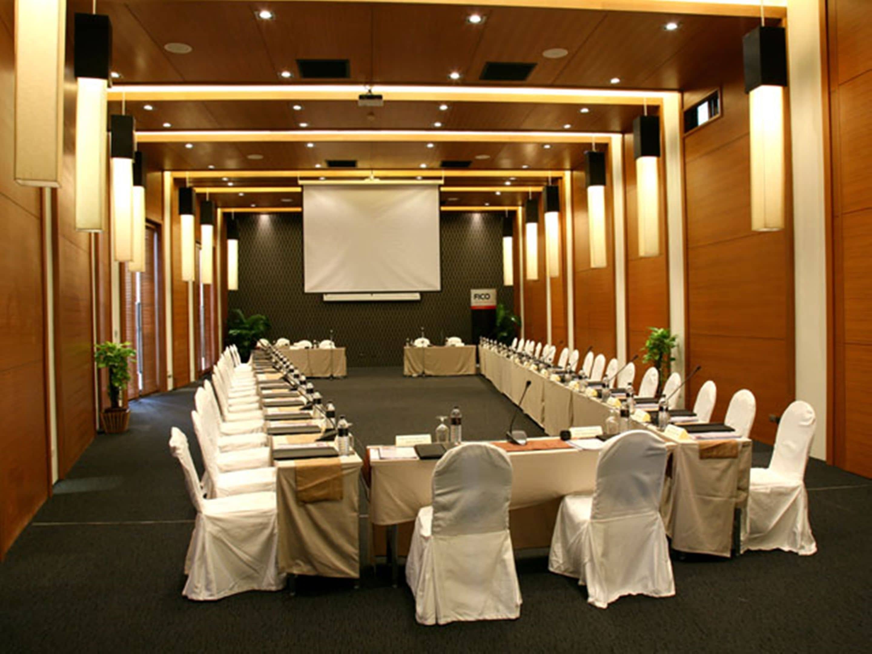 Een vergaderzaal met een lange tafel, stoelen en een projectiescherm.