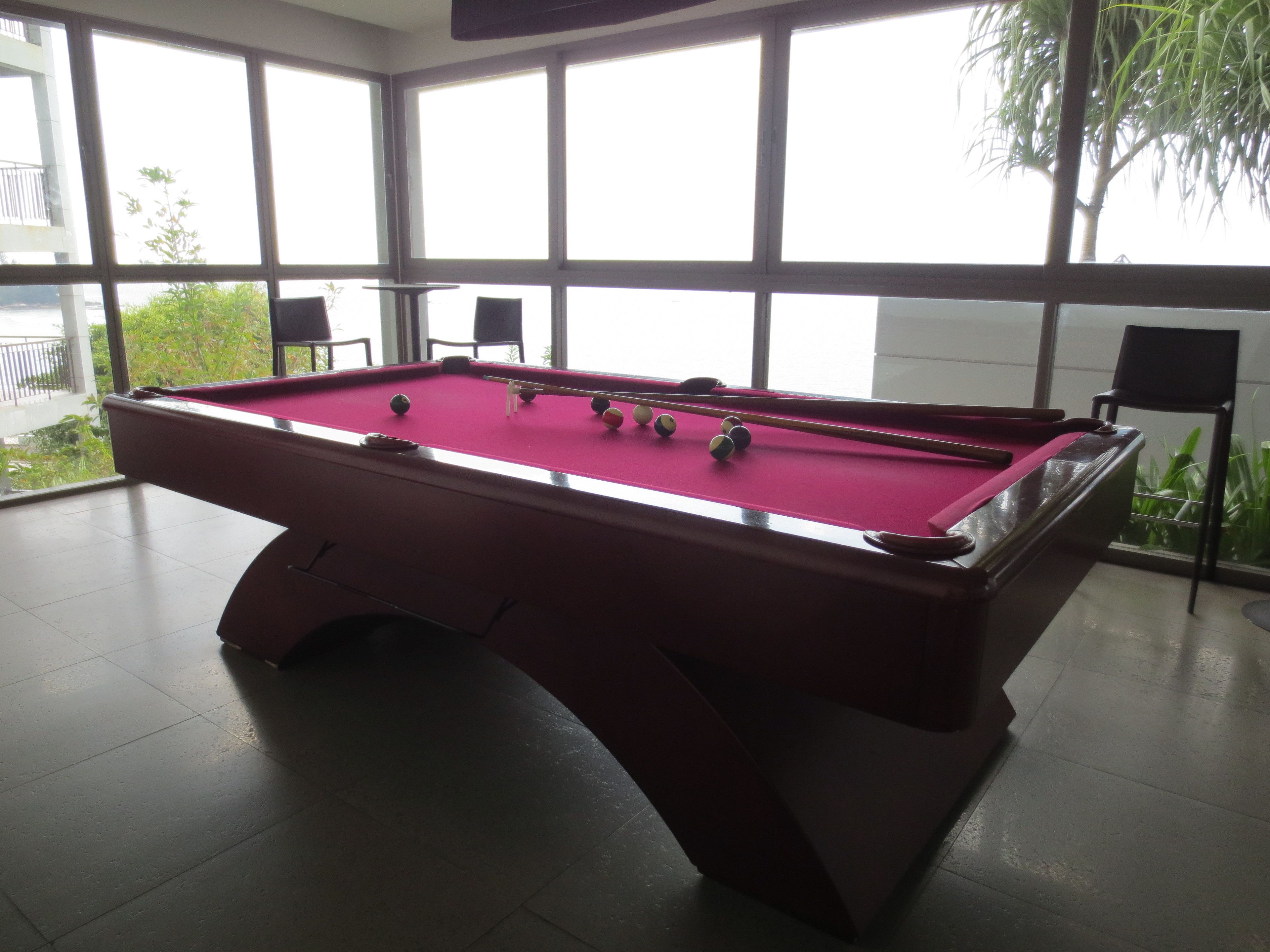 A pool table in a room with large windows and a view of greenery outside.