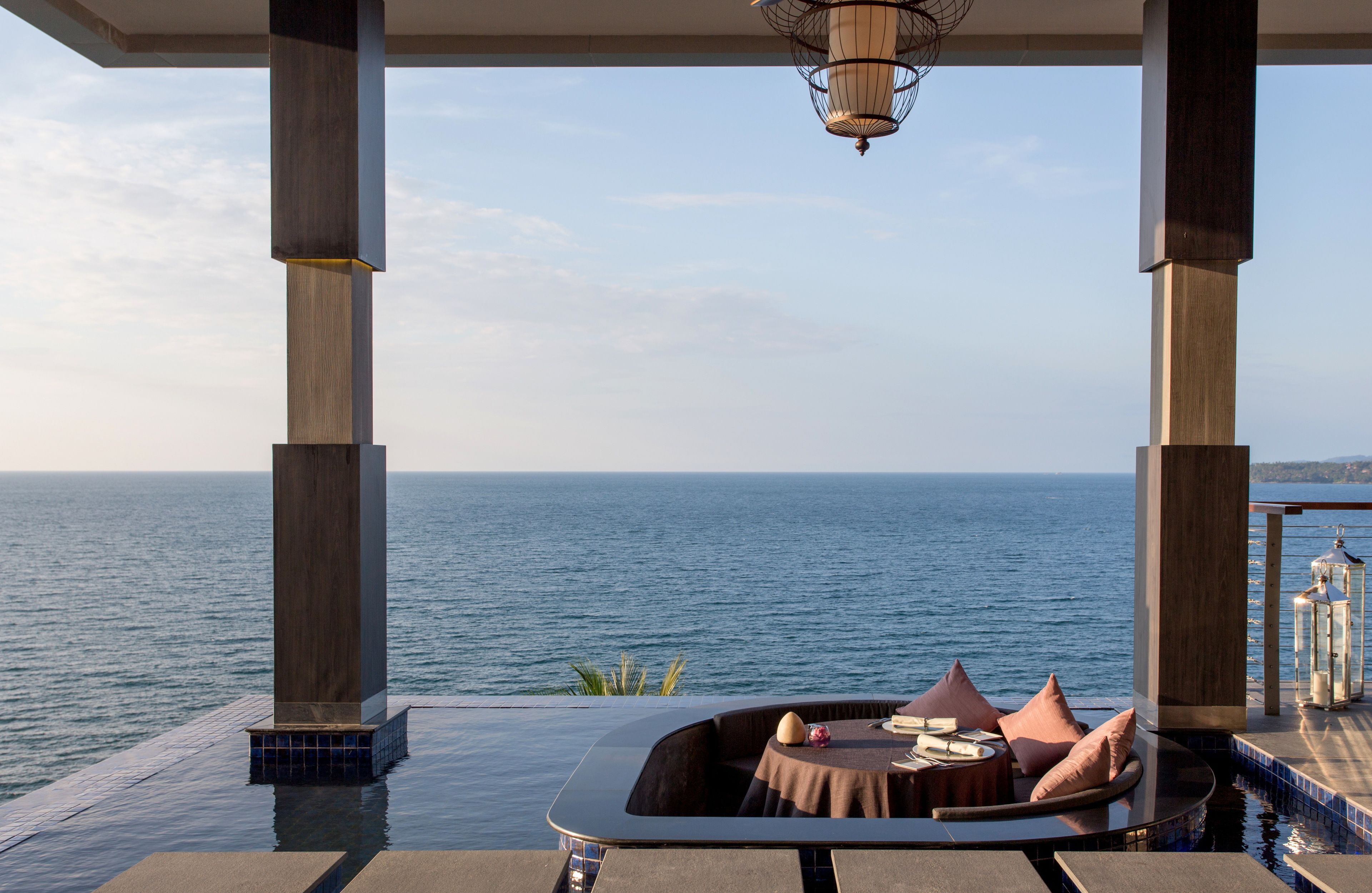 Un área de estar exterior lujosa con vista al mar, que incluye una mesa redonda y cojines.