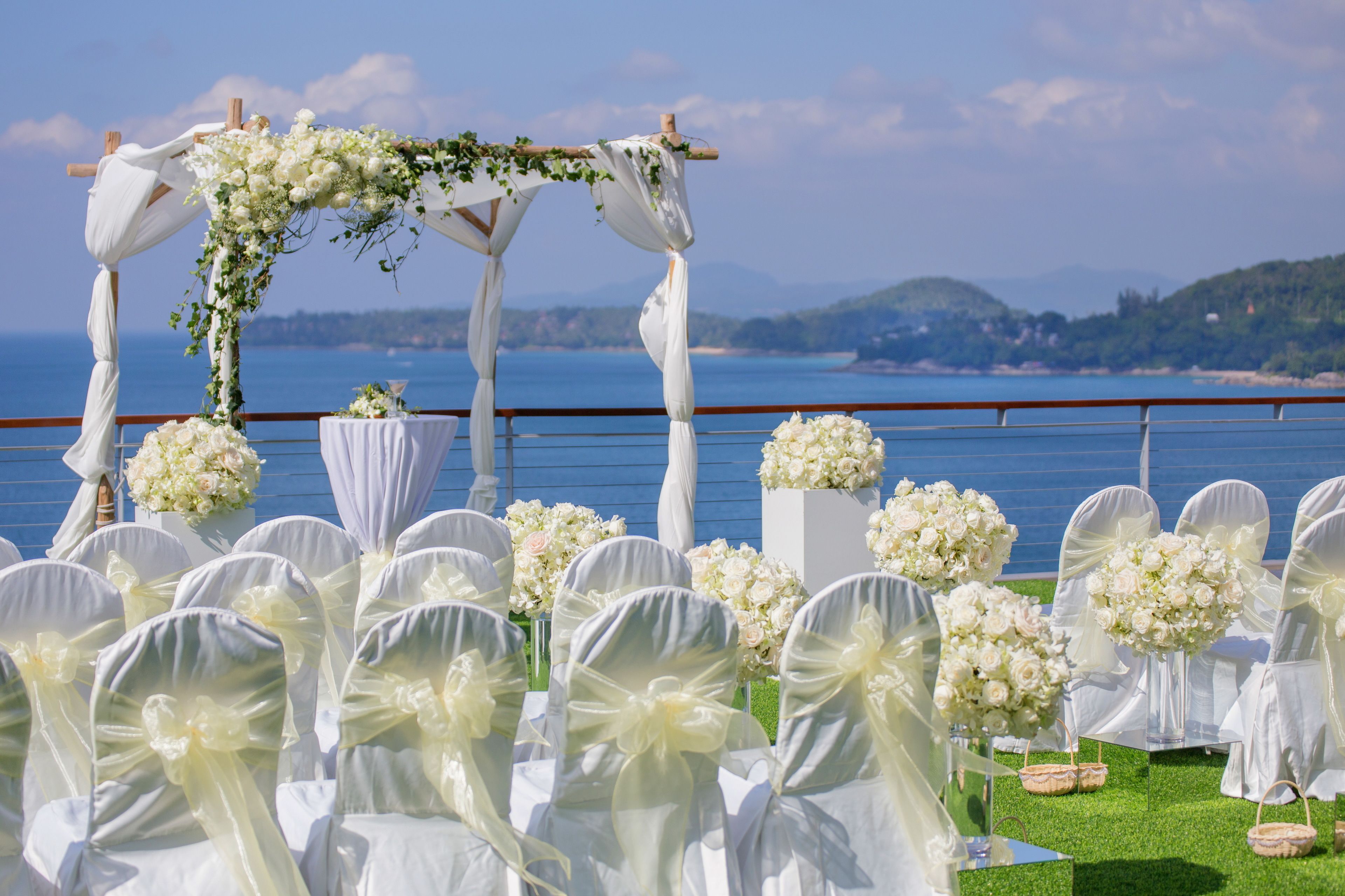 Hochzeitszeremonie mit weißen Stühlen und floralen Dekorationen vor einer schönen Kulisse.