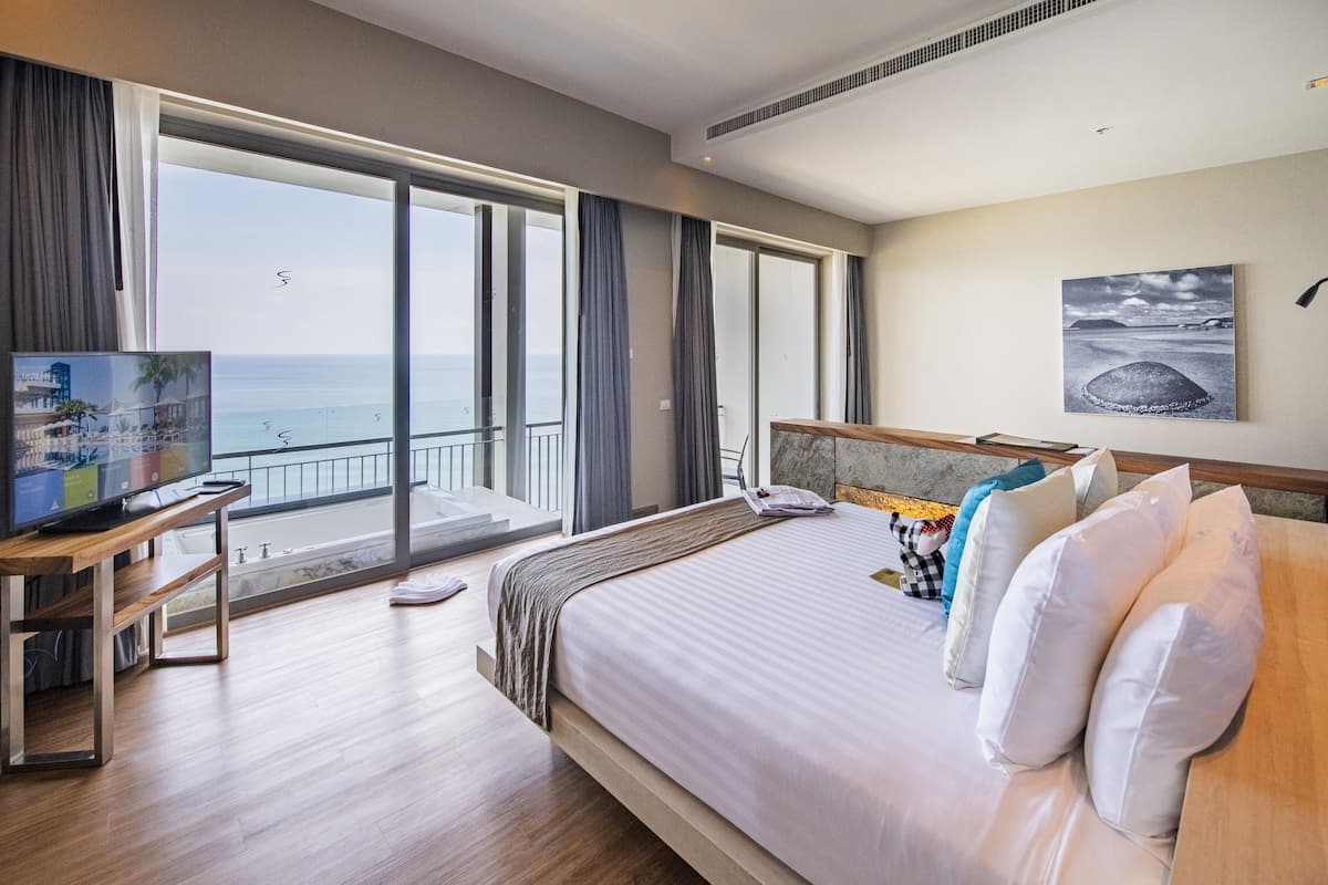 Habitación de hotel con una cama grande, un televisor sobre un soporte de madera, un balcón con vistas al mar y un cuadro en la pared.