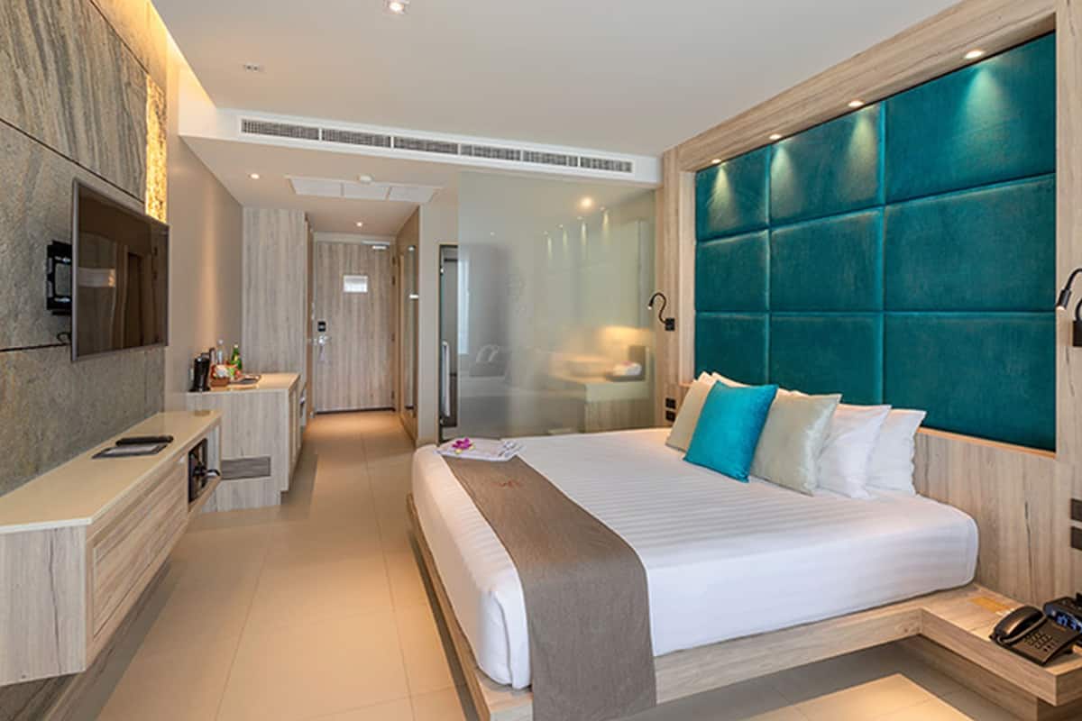 A modern hotel room with a large bed, a desk, a TV, and a bathroom.