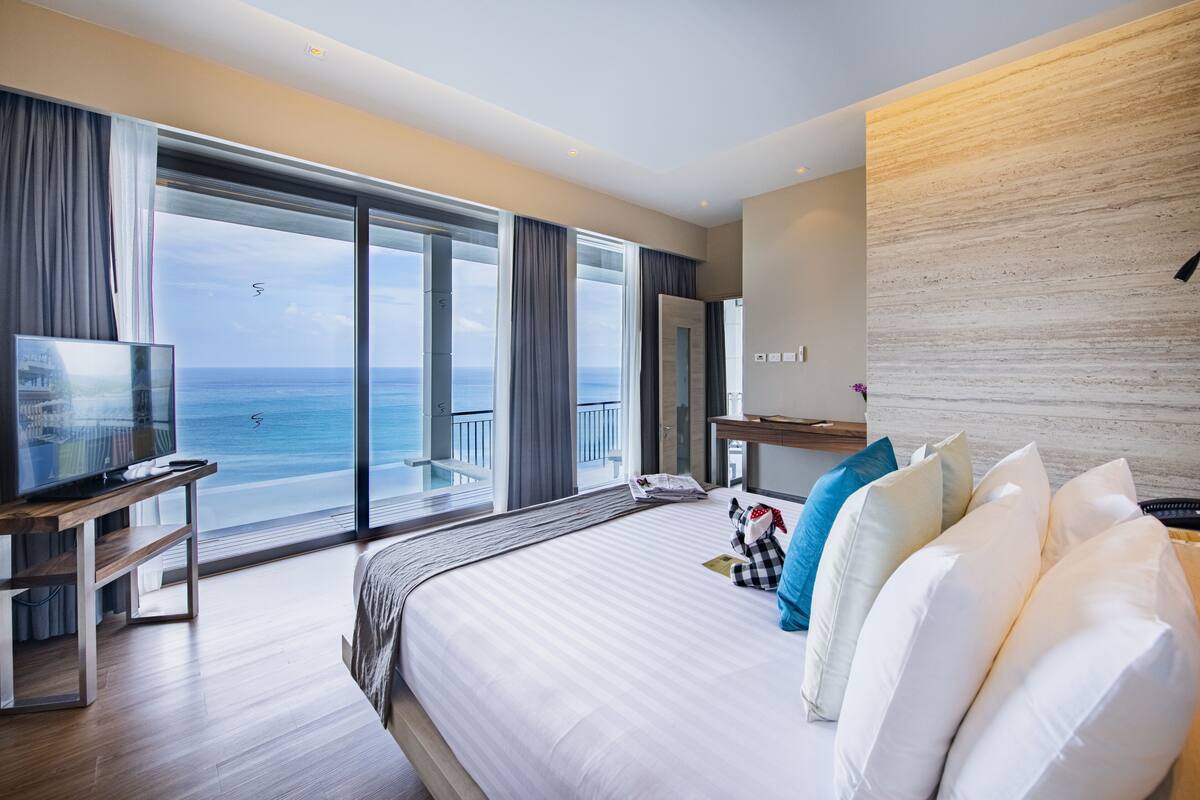 Habitación de hotel moderna con una cama grande, televisión, escritorio y balcón con vistas al mar.