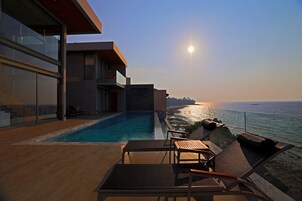Un área moderna junto a la piscina con sillones de descanso y vistas al océano.