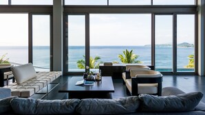 Un salon moderne offrant une vue imprenable sur l’océan, avec un canapé, des fauteuils et une table basse.