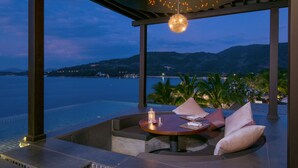 Une terrasse avec une table ronde et des coussins, d’où l’on a vue sur un plan d’eau et des collines.