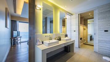 A modern bathroom with dual sinks, a large mirror, and a view of the sea.