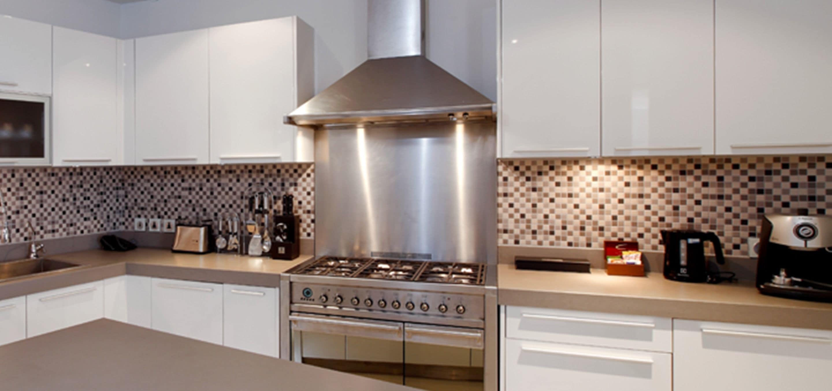 Una cocina moderna con armarios blancos, extractor de acero inoxidable y salpicadero de azulejos.