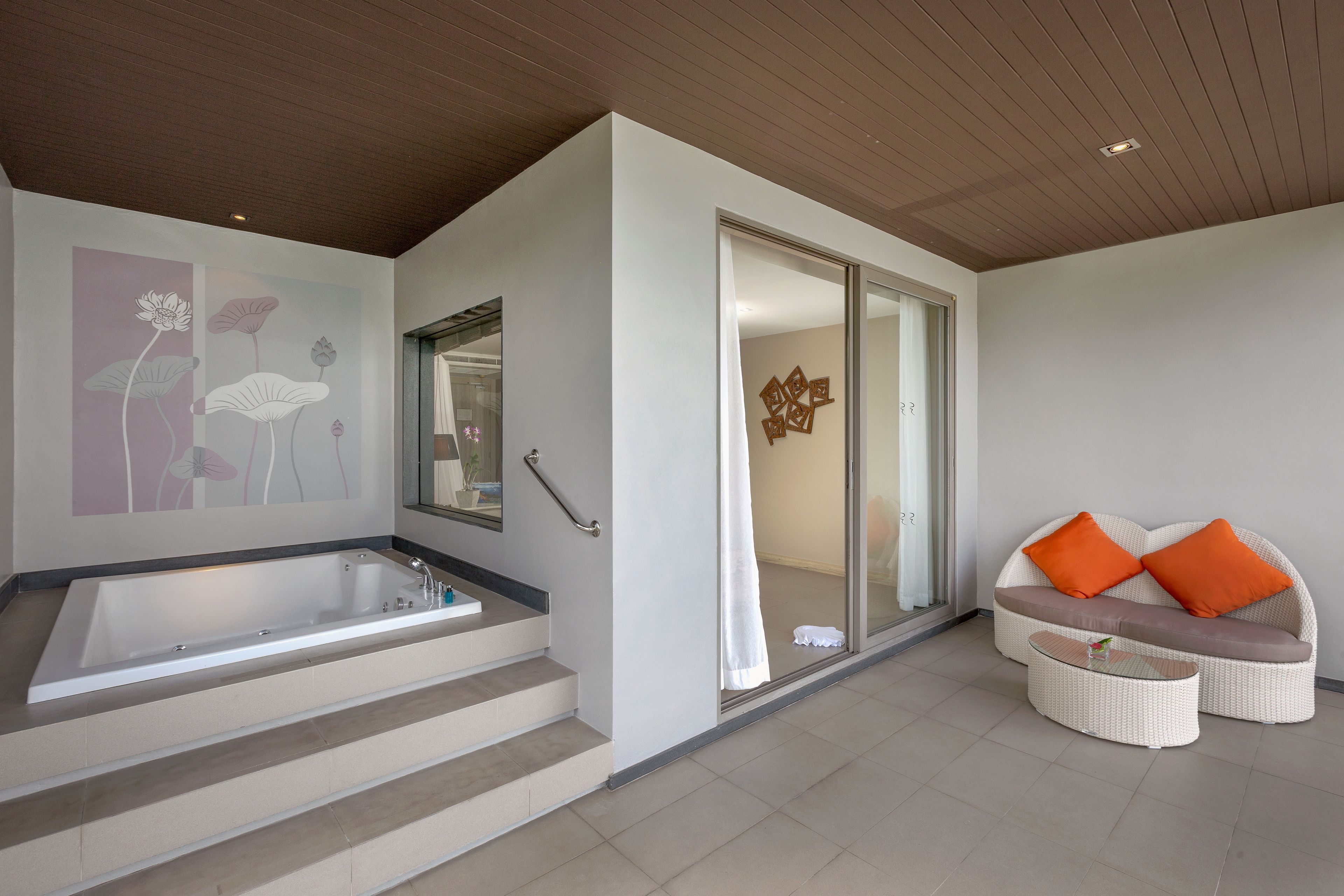 Une salle de bain moderne avec une grande baignoire, une cabine de douche en verre et un canapé blanc agrémenté de coussins orange.