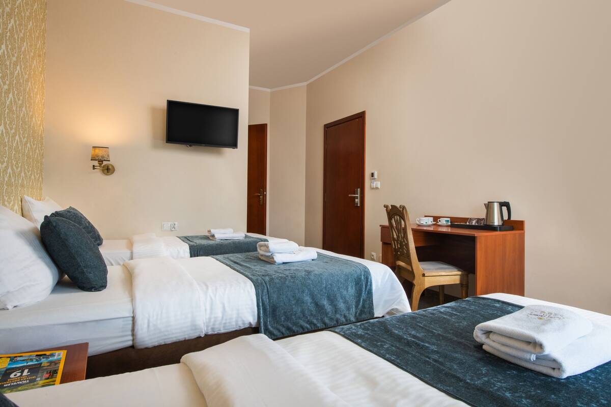 A hotel room with two beds, a desk, a chair, a television, and a wall-mounted lamp.