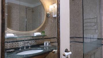 A bathroom with a round mirror, a sink with a marble countertop, a glass shower enclosure, and a tiled shower wall.