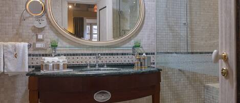 Un baño con lavamanos de mármol, un espejo grande y zona de ducha.