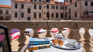 Un balcón con una mesa dispuesta para una comida, libros y vistas a edificios históricos.