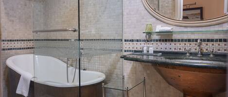 Un baño con ducha envuelta en vidrio, una bañera independiente y un lavamanos de cobre con espejo.
