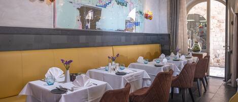 A restaurant with tables set for dining, a large decorative wall, and a view through an arched doorway.