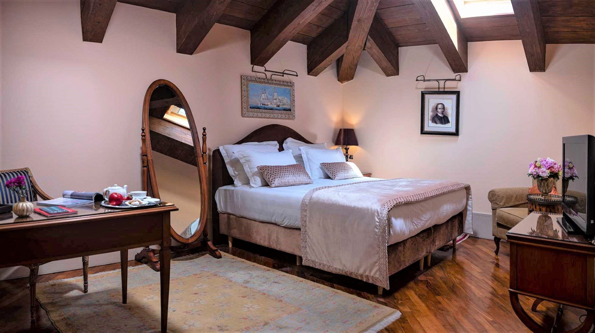 A bedroom with a bed, a desk, a mirror, a dresser, and a television.