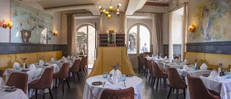 Un restaurant doté de nombreuses tables, de chaises marron à coussins moelleux et d’un bar central.