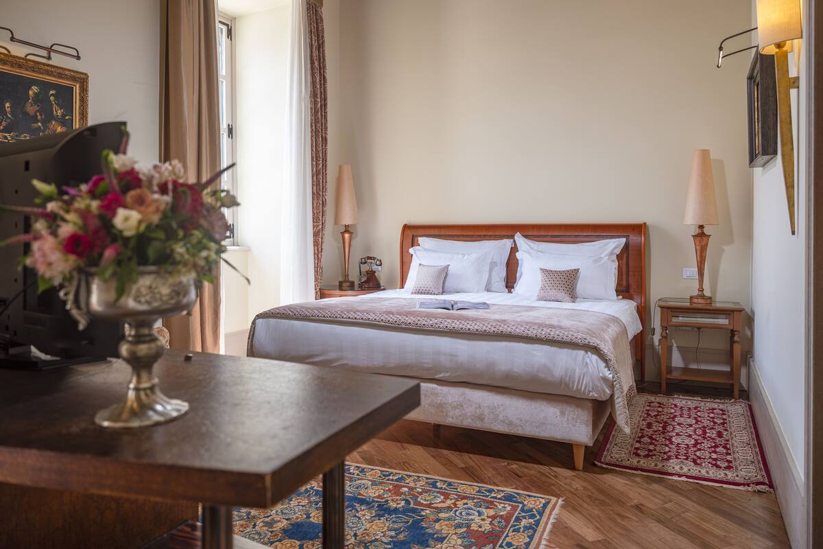 A neatly arranged bedroom with a wooden bed, bedside lamps, a floral vase, and a patterned rug.