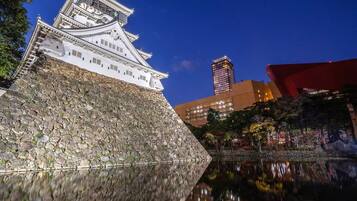 A traditional Japanese castle with a stone base and white walls, reflecting in a calm body of water.