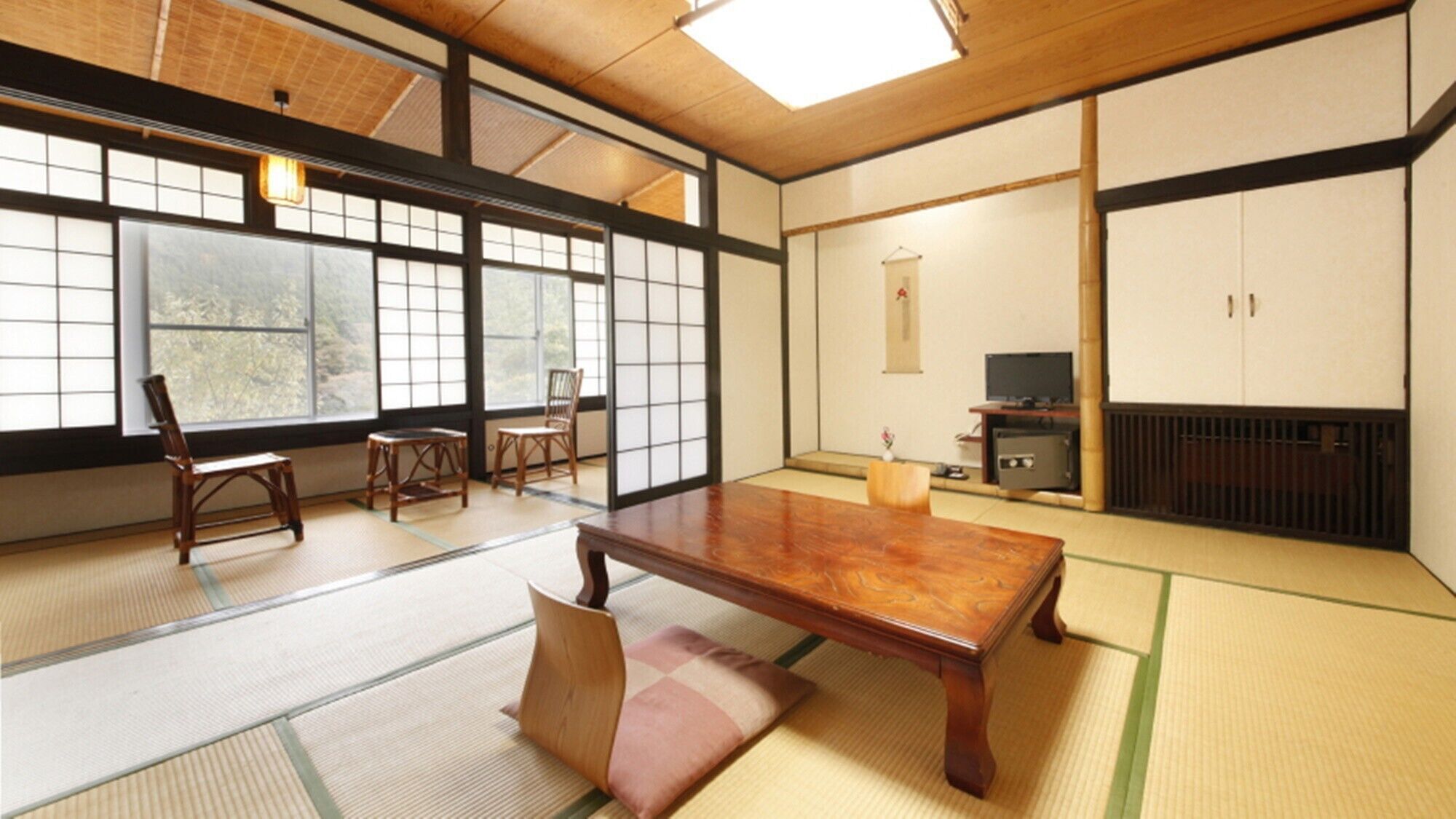 A traditional Japanese room with tatami flooring, a low table, chairs, and a television.