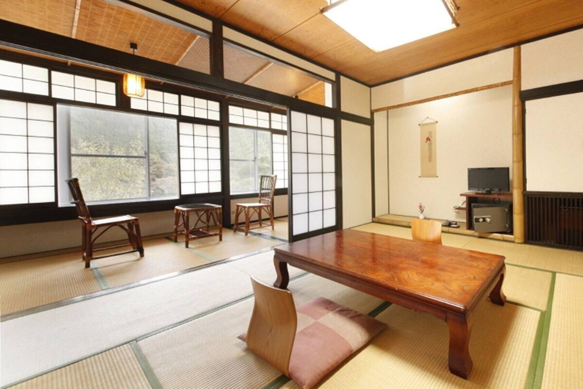 A traditional Japanese room with tatami flooring, a low table, chairs, and a television.