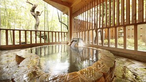 A traditional Japanese onsen with a stone bath, wooden railings, and a view of bamboo trees. - The Aizuya (Nasushiobara)