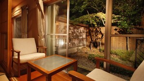 A cozy patio area with a wooden table and chairs, a glass door leading to a garden with a wooden fence and trees. - The Aizuya (Nasushiobara)