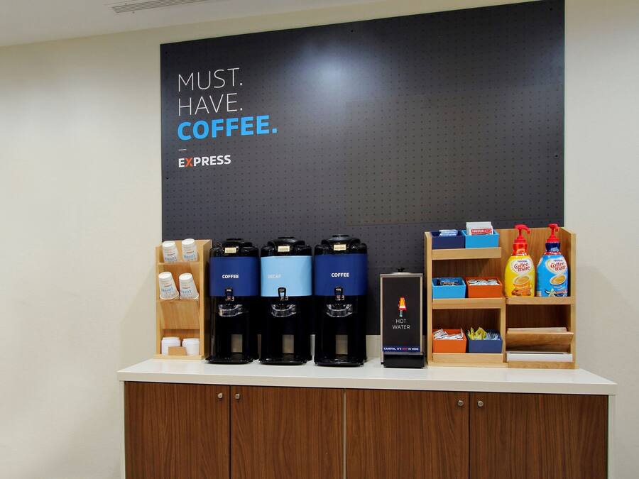 Een koffiehoek met meerdere koffieautomaten, een heetwaterdispenser en een bord waarop staat 'MUST. HAVE. COFFEE.'