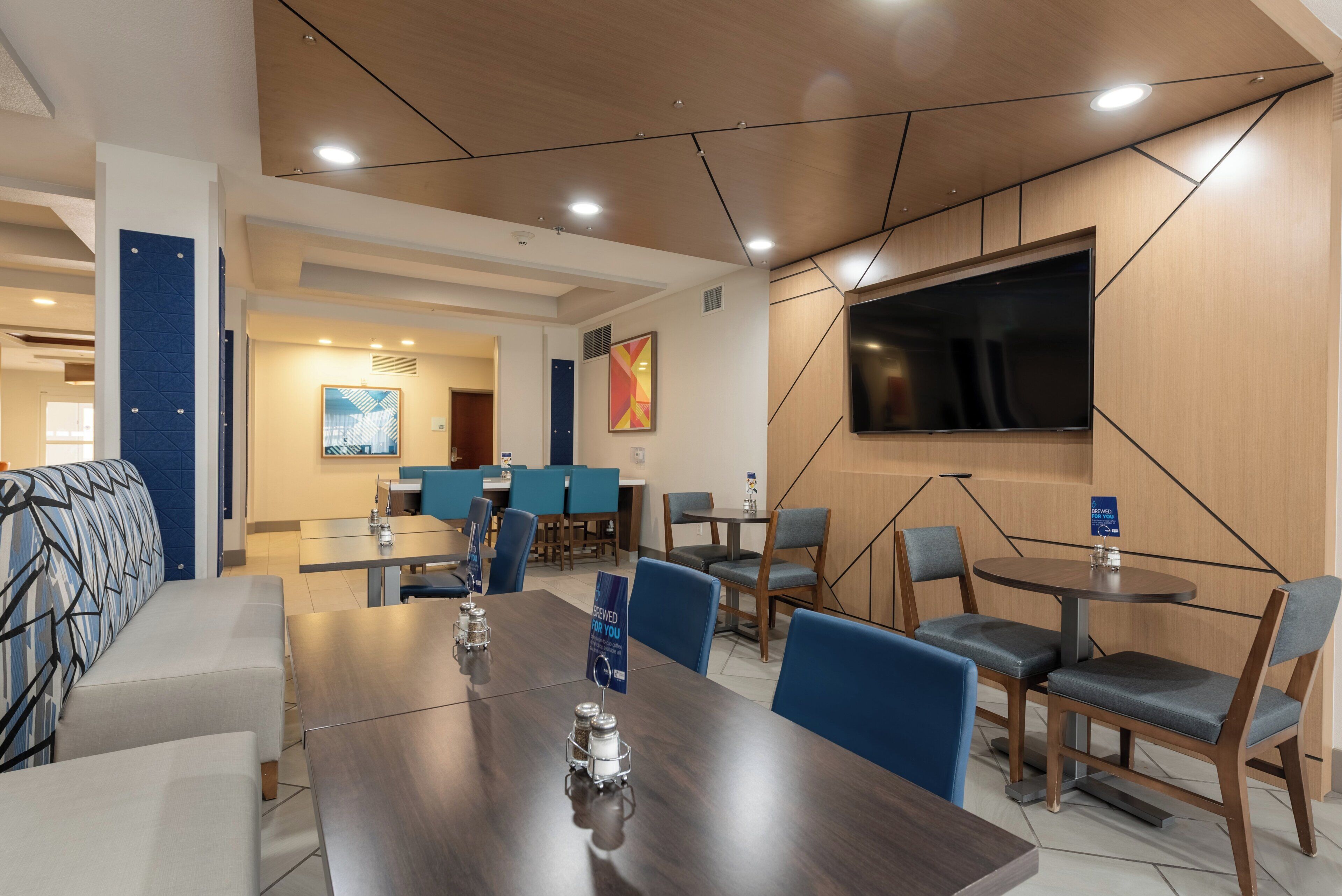 A modern conference room with a large table, chairs, a flat-screen TV, and a blue accent wall.