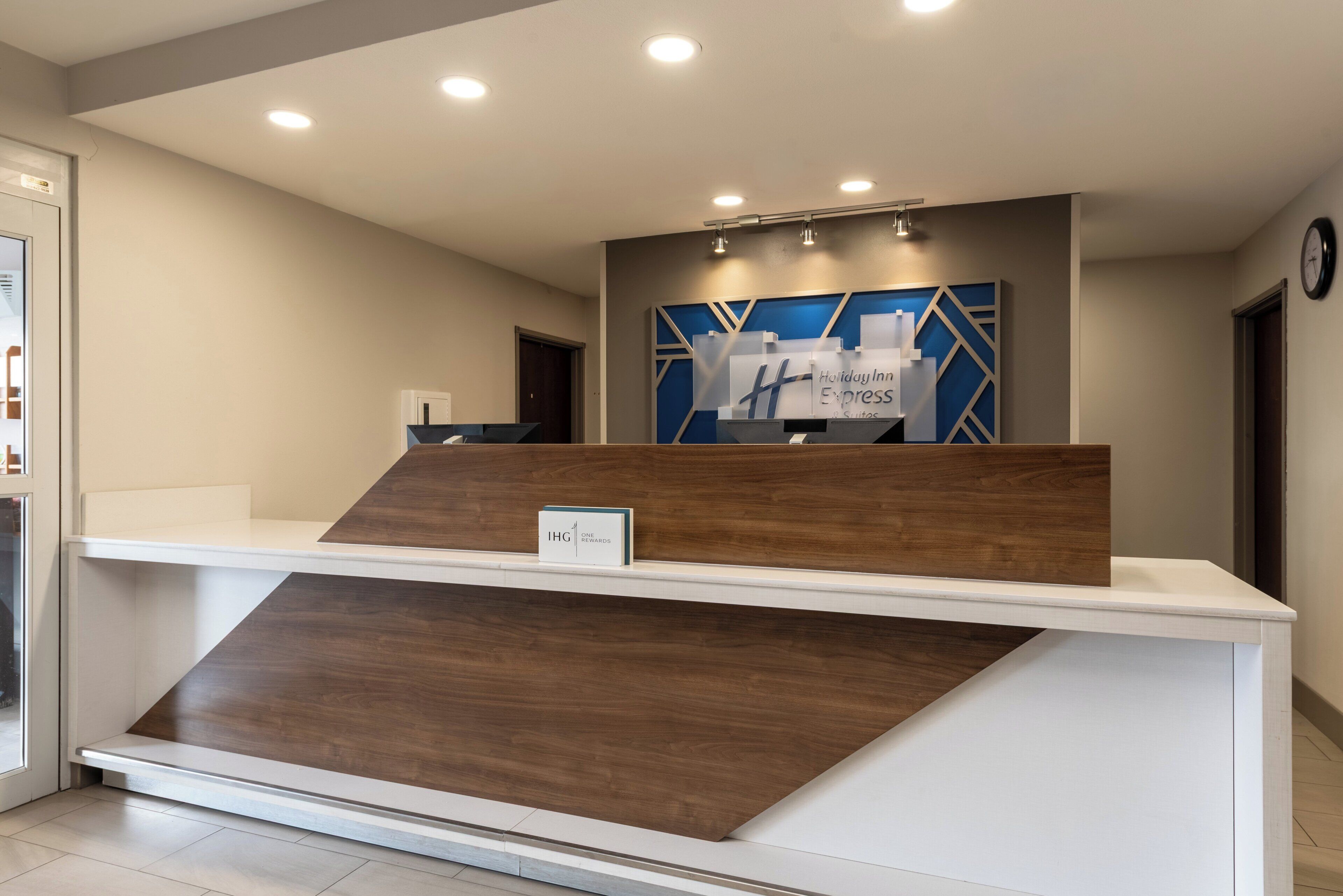 A reception desk with a sign for Holiday Inn Express & Suites, a clock, and a modern design with recessed lighting.