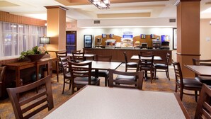 A hotel dining area with wooden tables and chairs, a buffet counter, and a large window with curtains.