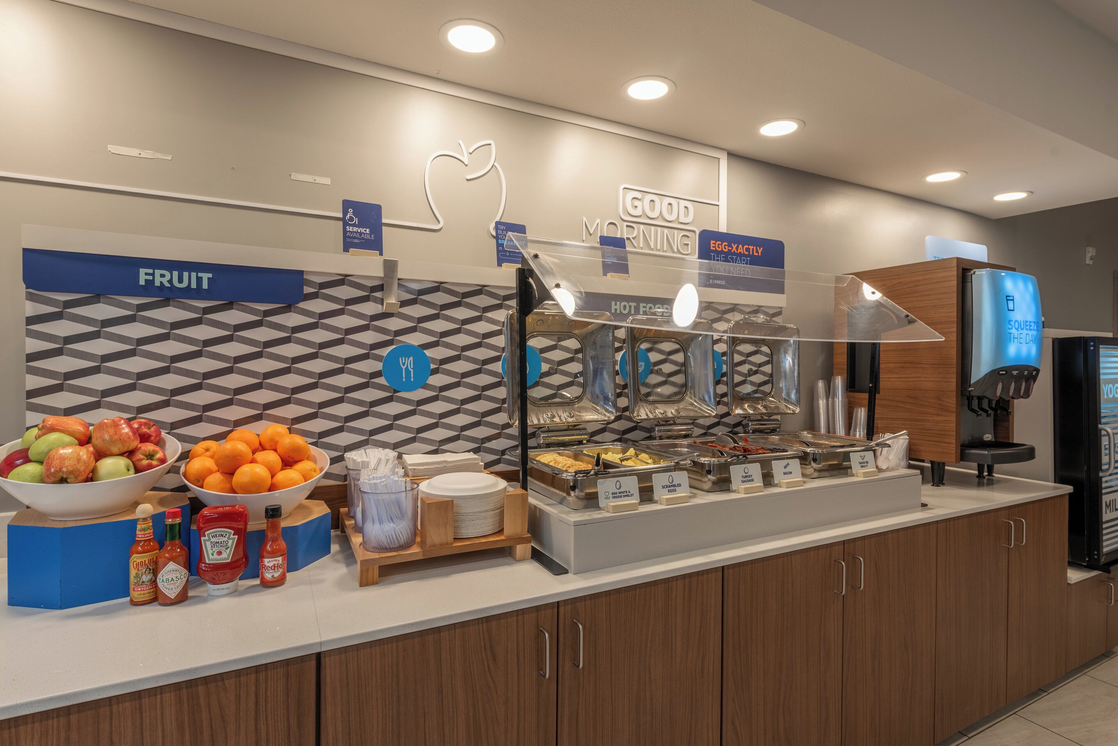 Un espace buffet pour le petit-déjeuner avec des présentoirs indiquant les différents types d’aliments, un saladier de fruits, des condiments et une machine à café.