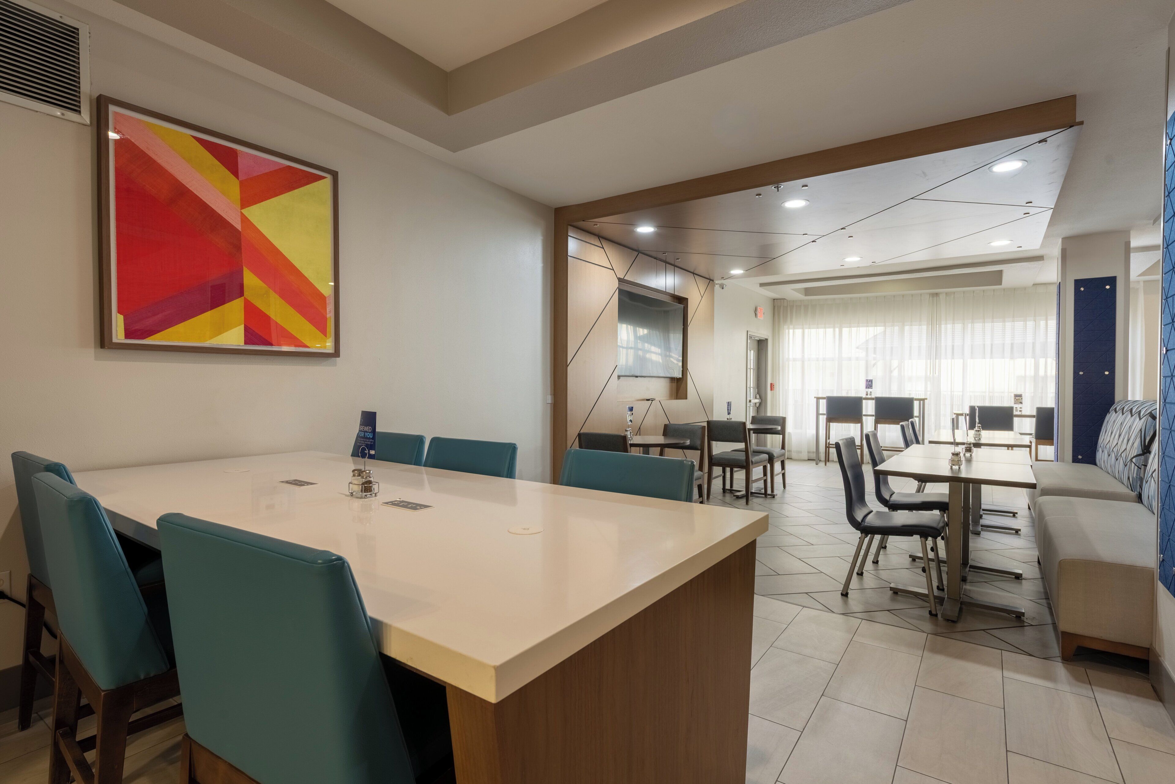 A conference room with a large table, chairs, and a colorful abstract painting on the wall.