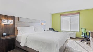A hotel room with a bed, bedside table, lamp, and a desk with a chair.