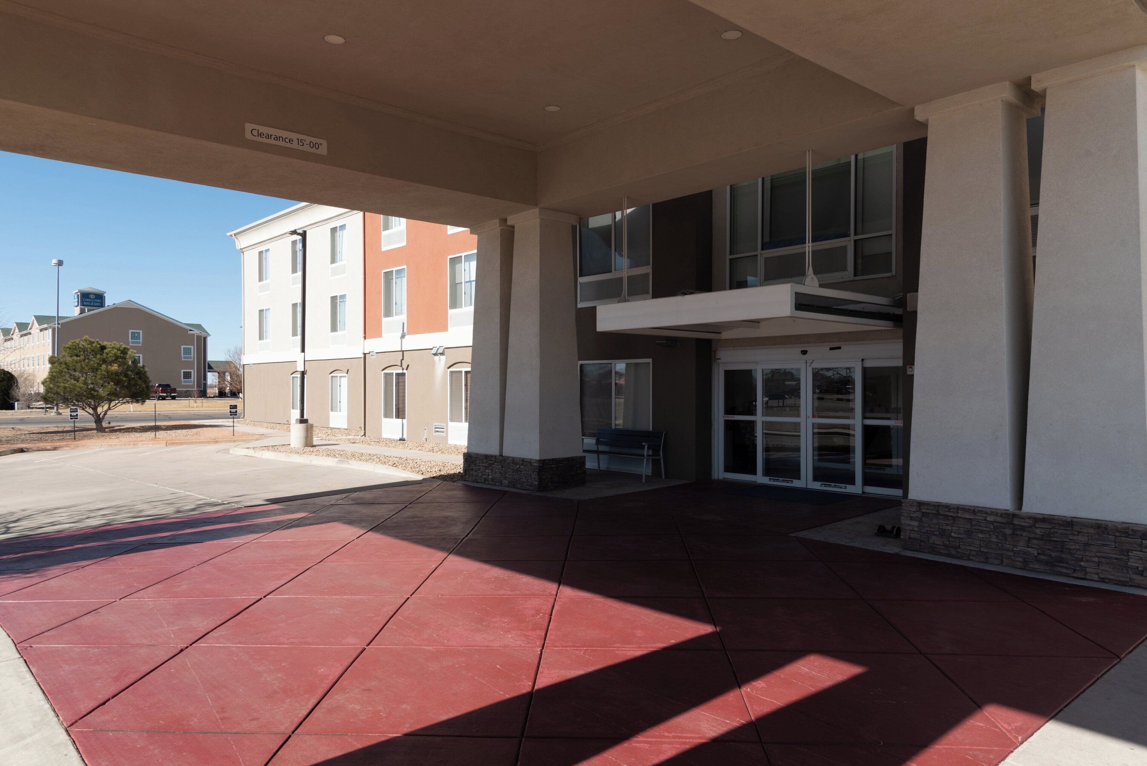 A building entrance with a red-tiled floor, a clear sky, and a sign indicating a clearance of 15'-00'.