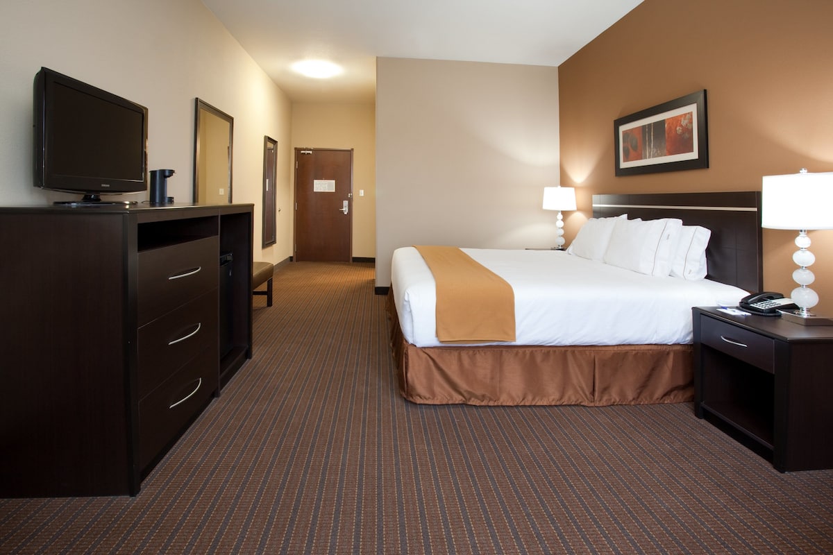 Une chambre d’hôtel comprenant un lit, un bureau avec une lampe, une télévision et une commode.