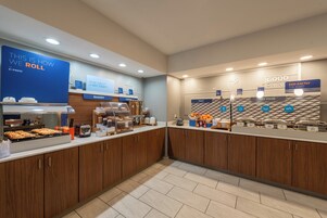 Zona de desayuno tipo bufé con secciones identificadas para panadería, cereales, fruta, comida caliente y huevos.