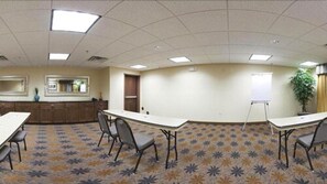 Une salle de conférence avec une longue table, des chaises, un tableau blanc et une plante.