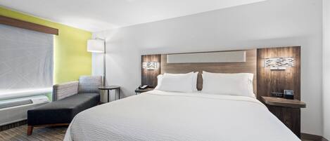 Habitación de hotel con una cama grande, mesitas de noche, un escritorio, una silla, un sofá y una ventana con persianas.