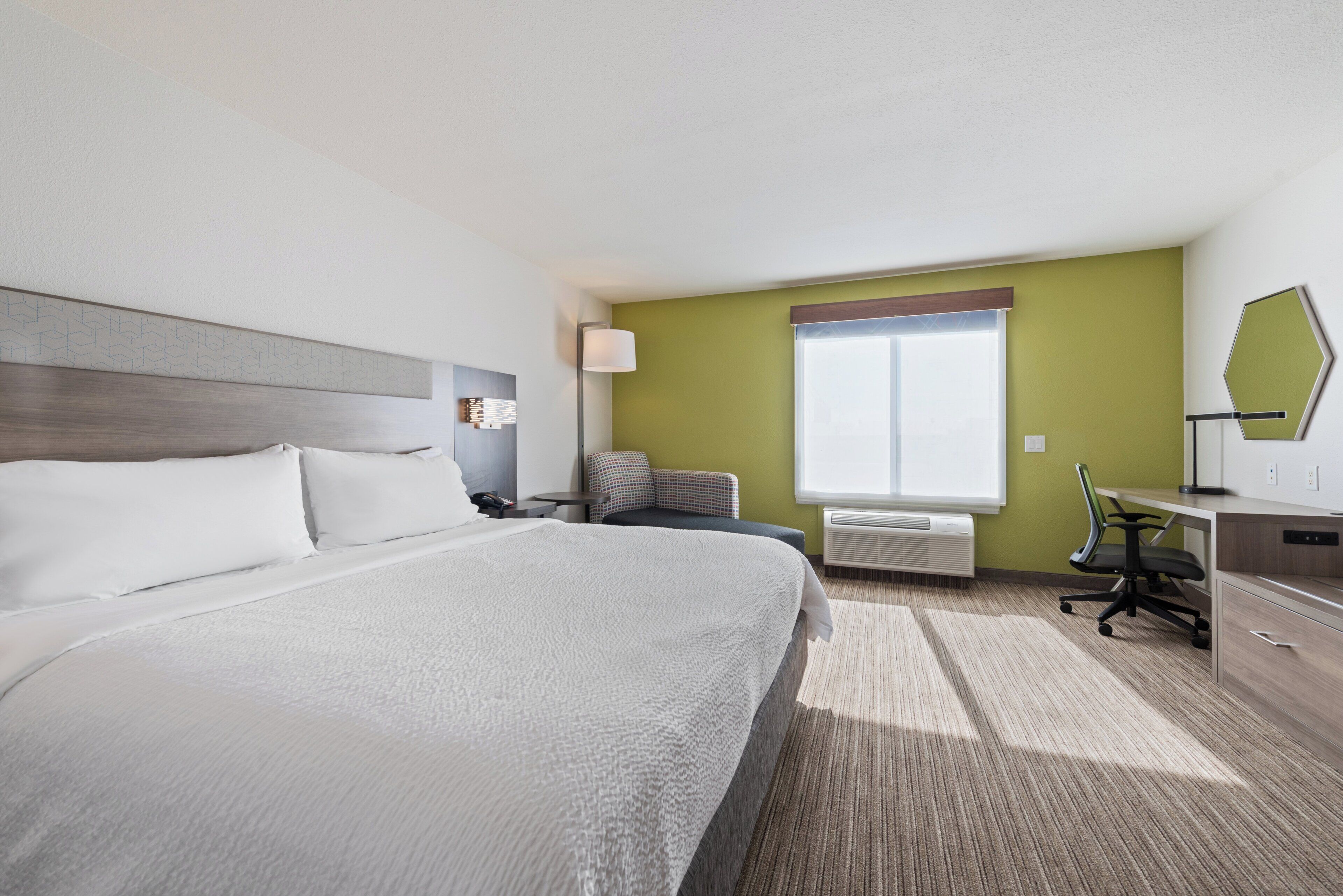 A hotel room with a large bed, a desk, a chair, a lamp, and a window.