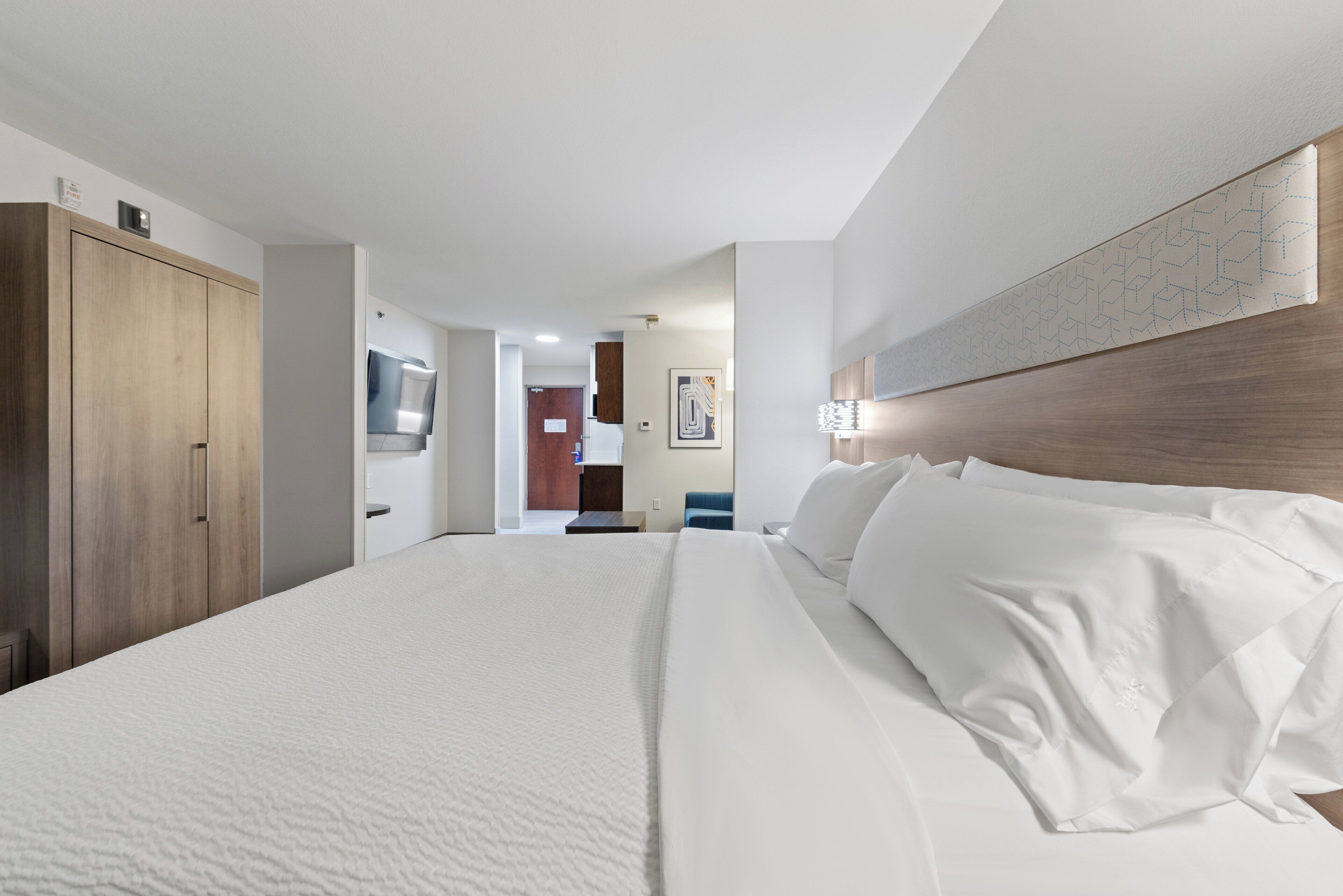 A hotel room with a large bed, a wardrobe, a bathroom with a mirror, and a hallway leading to another room.