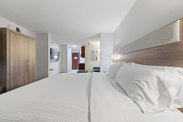 Habitación de hotel con una cama grande, un armario, un baño con espejo y un pasillo que conduce a otra habitación.