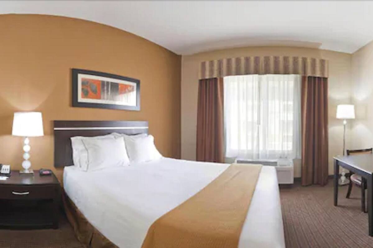 Habitación de hotel con una cama grande, un escritorio, una silla, una mesita de noche y una ventana con cortinas.