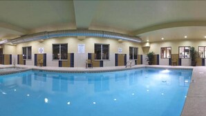 An indoor swimming pool with tiled walls, windows, and a few chairs.