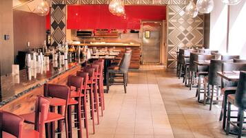 A restaurant interior with a bar area, multiple tables and chairs, and a modern kitchen in the background.