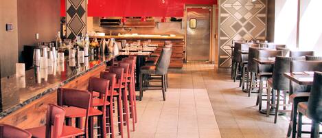 A restaurant interior with a bar area, multiple tables and chairs, and a modern kitchen in the background.