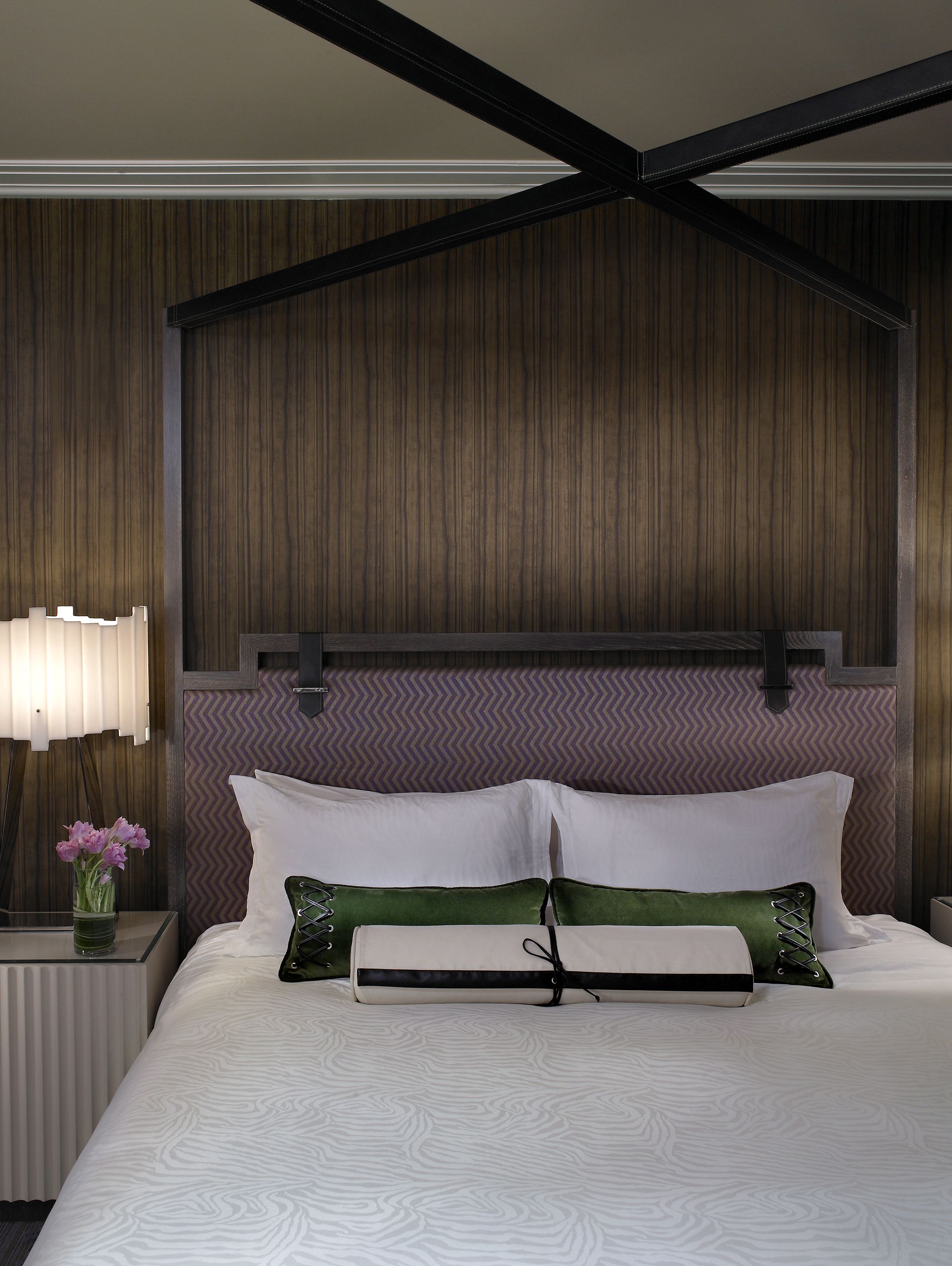 A hotel room with a bed, a nightstand, a lamp, and a wall with a herringbone pattern.